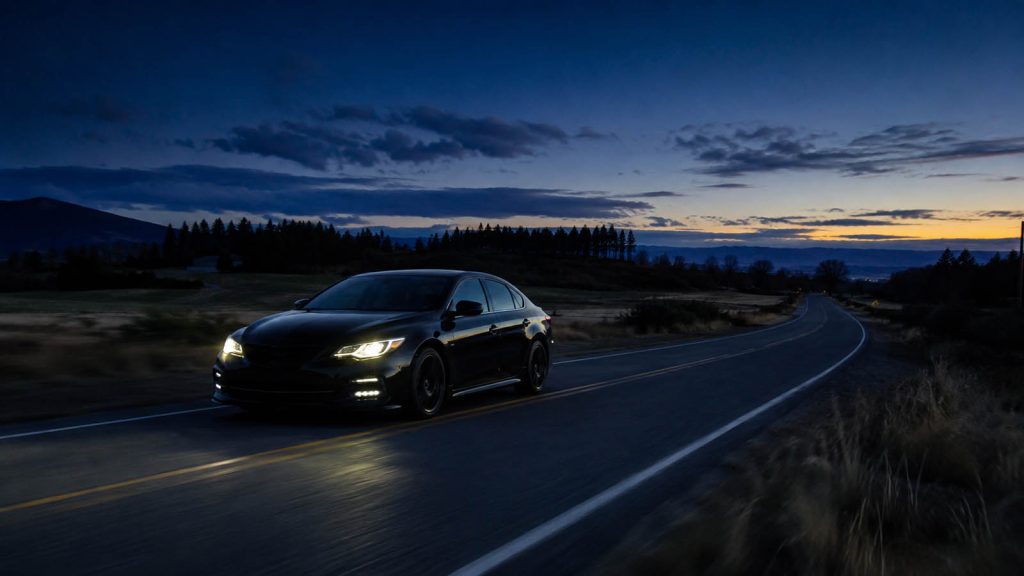 Black car traveling alone on a quiet rural road at blue hour