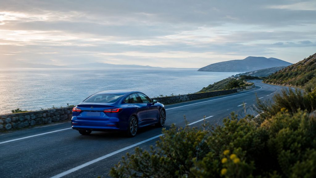 Blue car traveling along a quiet coastal road beside calm morning water